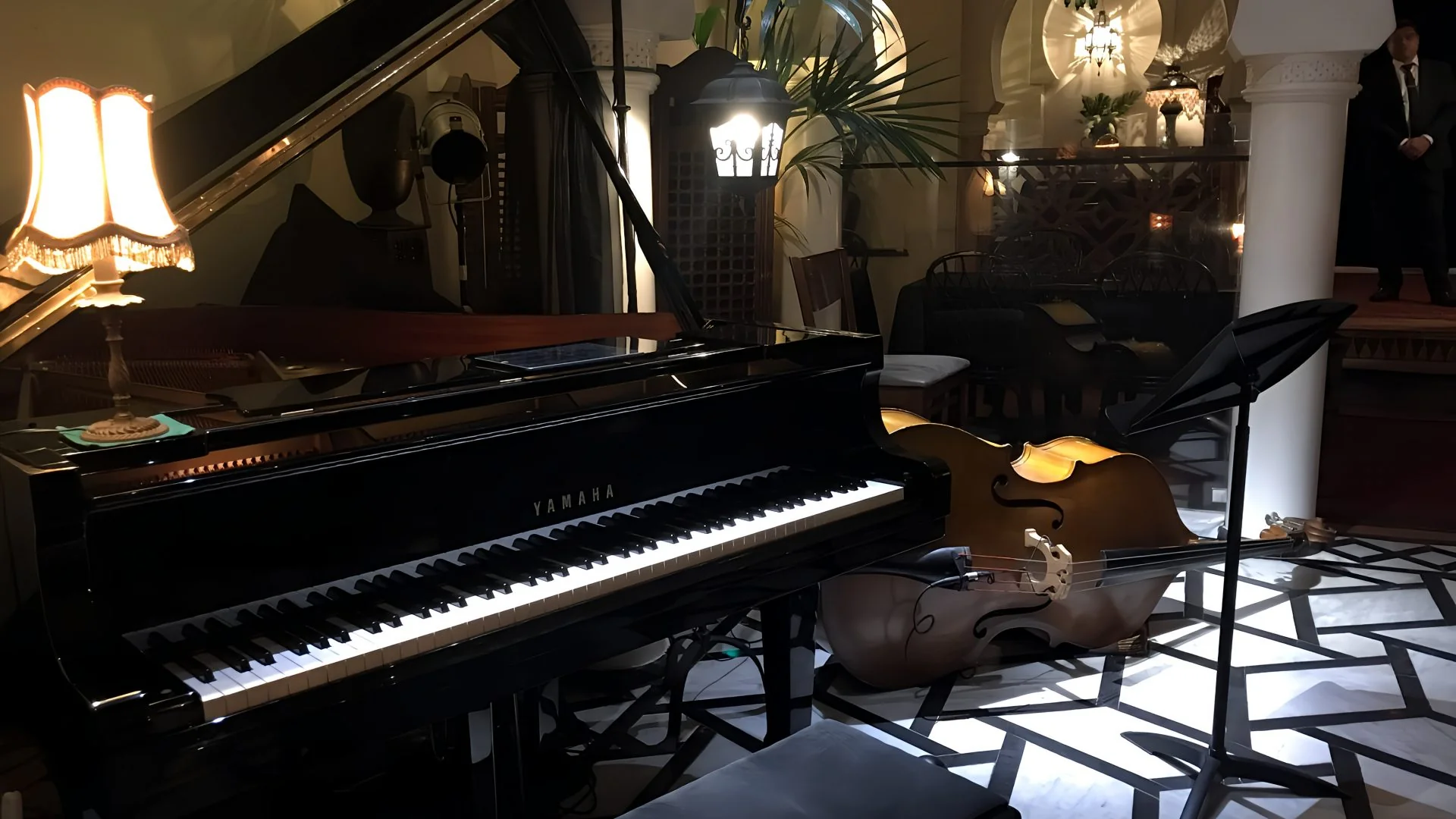 Close-up of the black lacquered grand piano keyboard, vintage lamp, and acoustic double bass