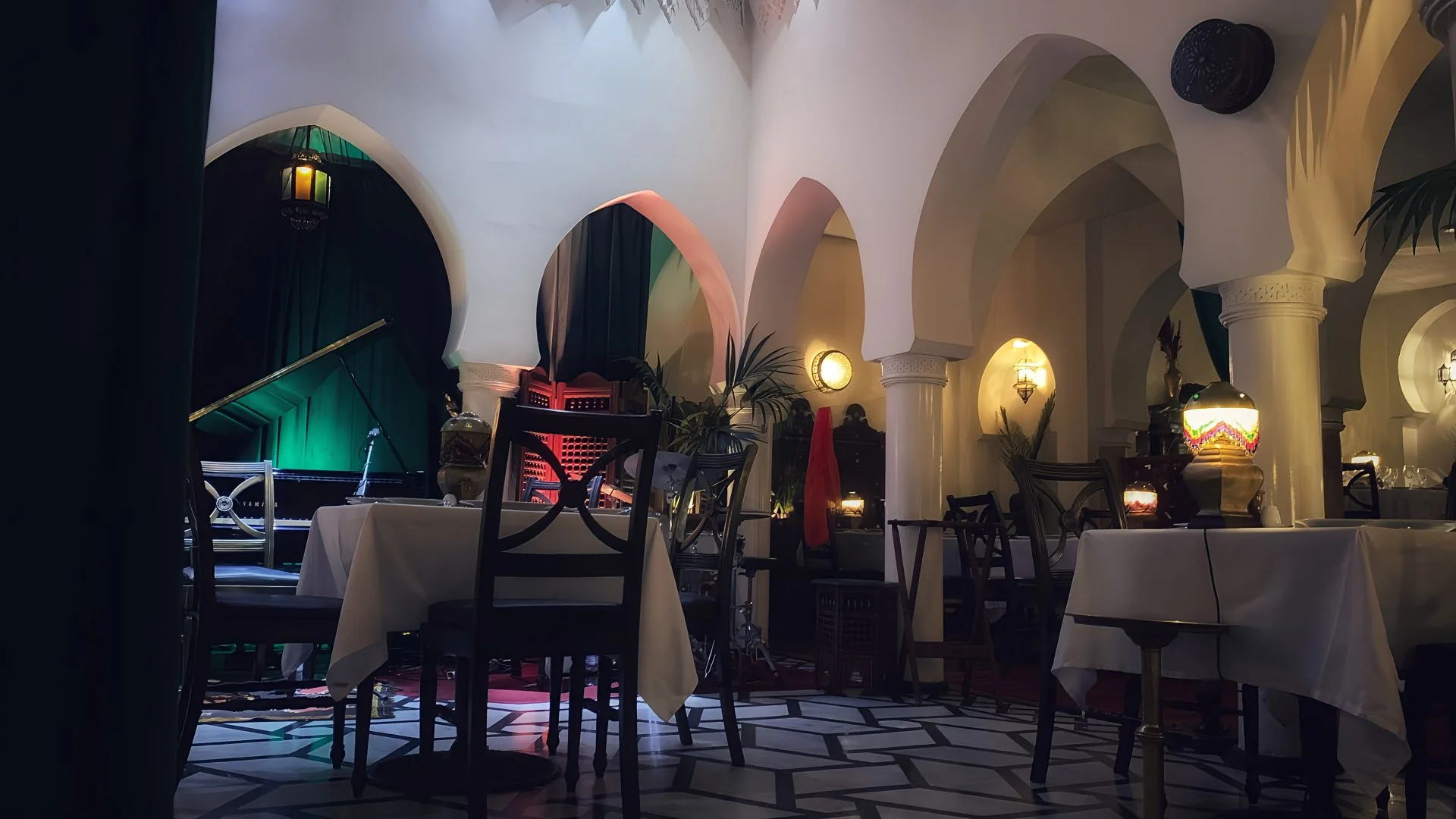 Courtyard dining tables with glowing table lamps and emerald stage lighting behind the grand piano
